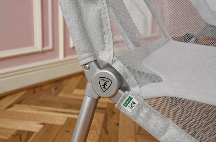 Gros plan sur la charnière pliable et le filet respirant d'un lit parapluie compact installé sur parquet en chevrons